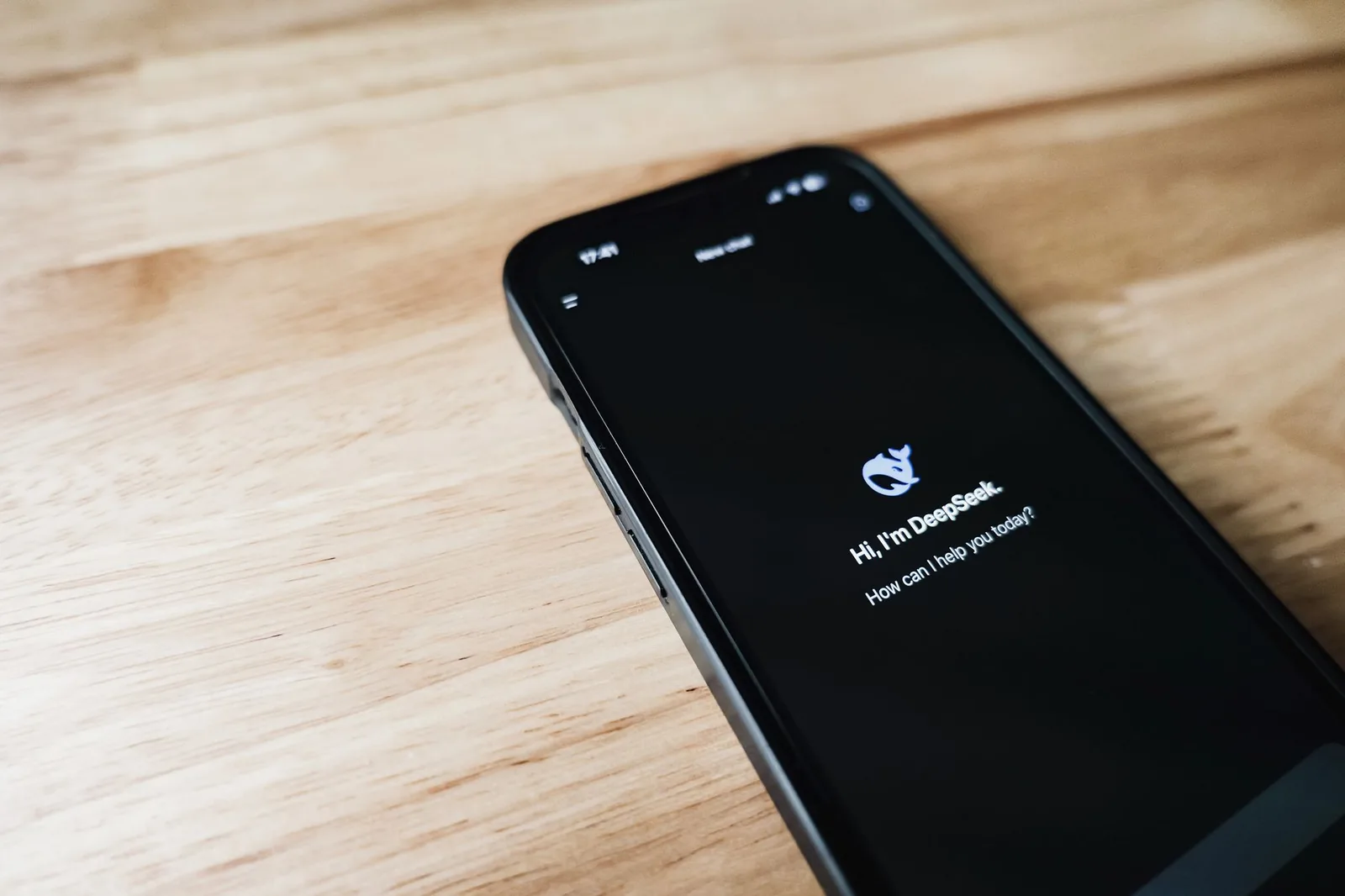 Close-up of a smartphone with DeepSeek virtual assistant on screen, placed on a wooden surface.