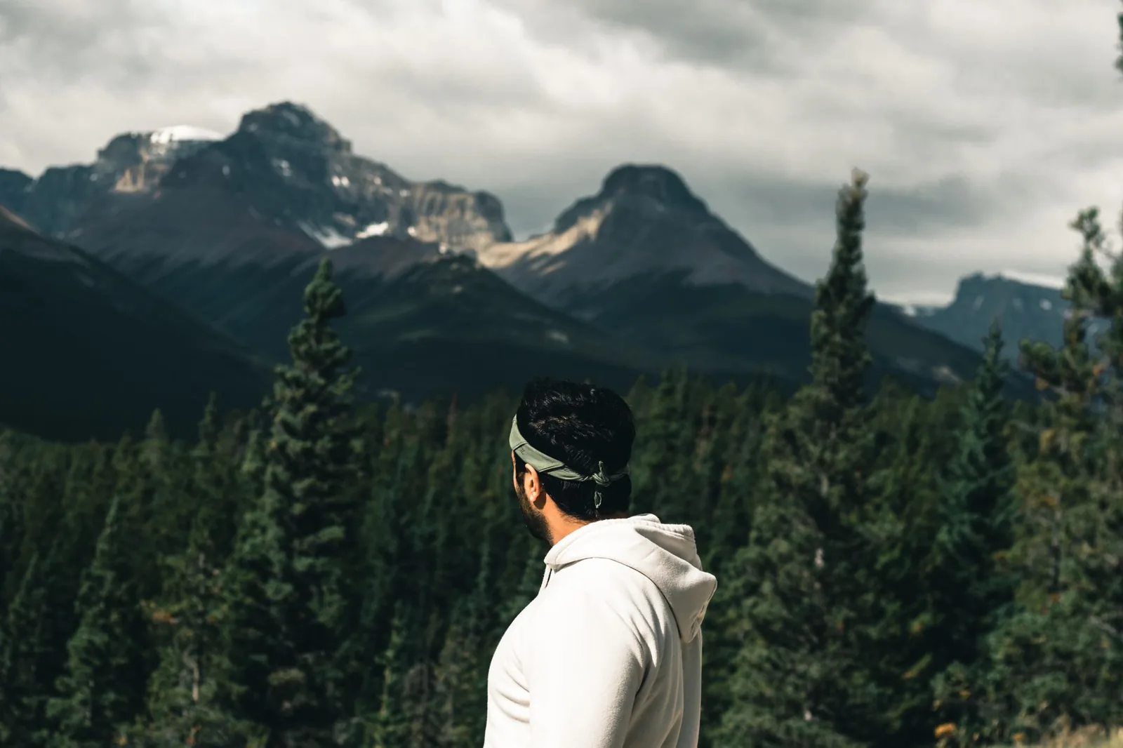A man in a white hoodie views the majestic Canadian Rockies under a cloudy sky in Jasper National Park.