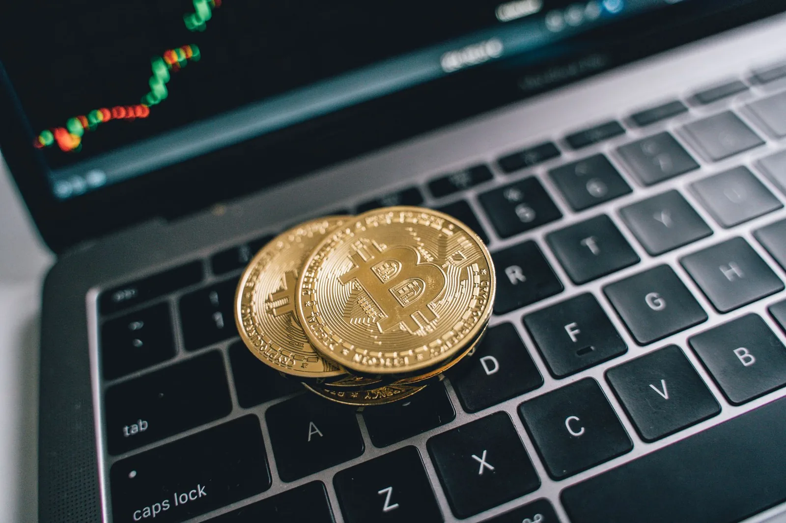 Close-up of golden bitcoins on a laptop keyboard depicting cryptocurrency and trade concepts with a market chart in the background.