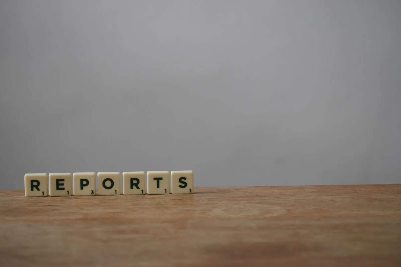 Scrabble tiles spelling 'reports' on a wooden desk, ideal for office or business themes.