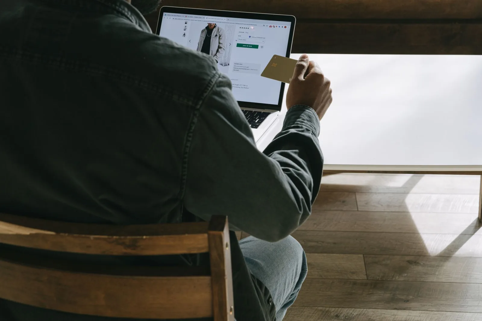 Adult man using a laptop while holding a credit card for online shopping in a comfortable indoor setting.