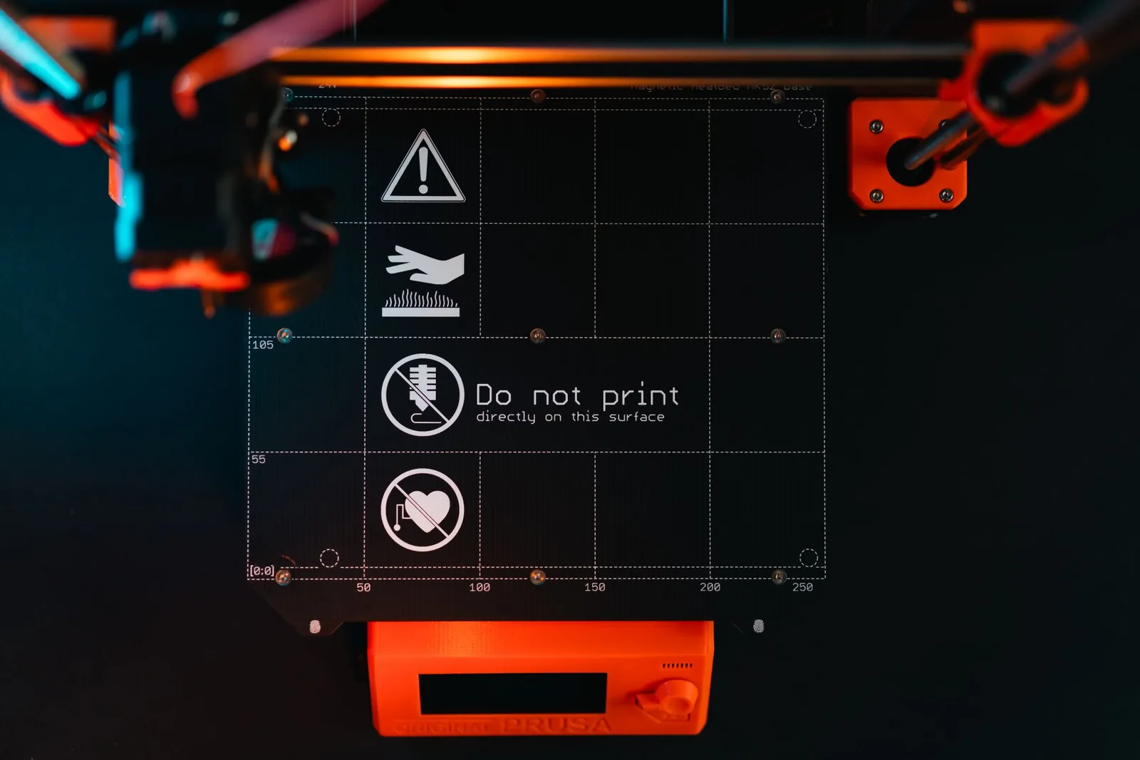 3D printer build plate with warning symbols, showcasing high-tech equipment in a workspace.