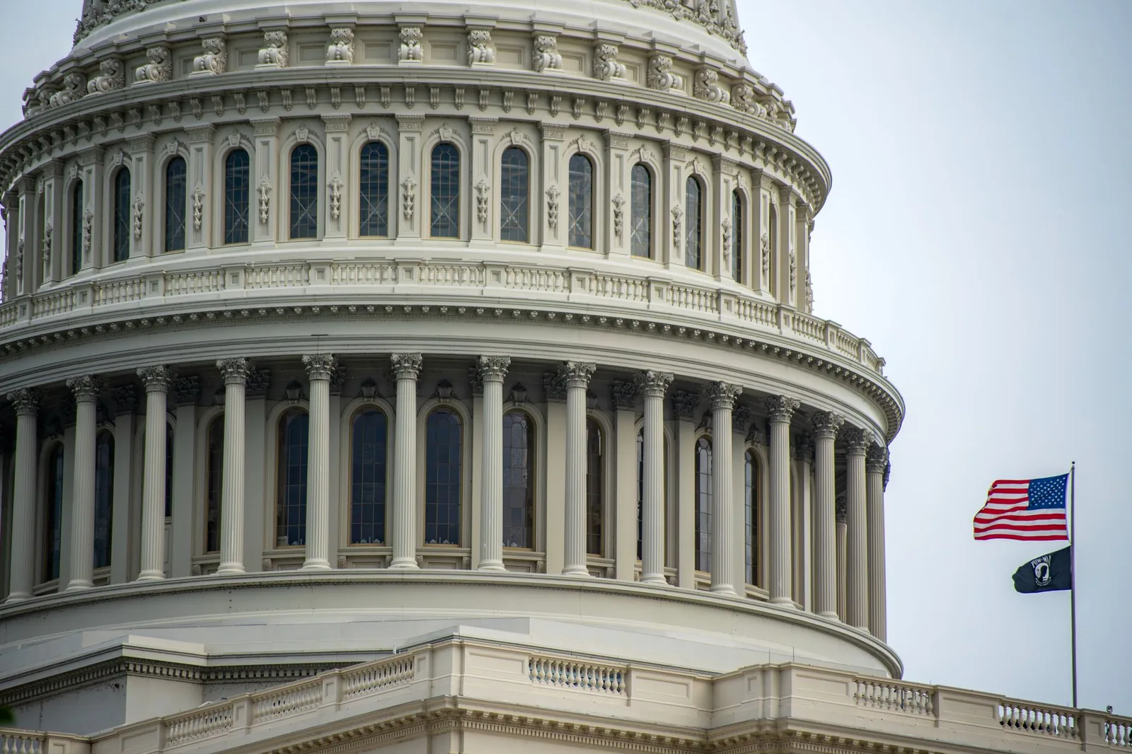 Detail of the US Capitol dome in Washington, D.C., featuring an American flag waving beside it.